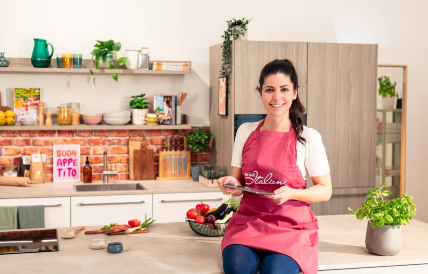 Serena Loddo sitzt auf der Kücheninsel in der So isst Italien Küche und sucht auf dem Tablet nach Rezepten für Ostern