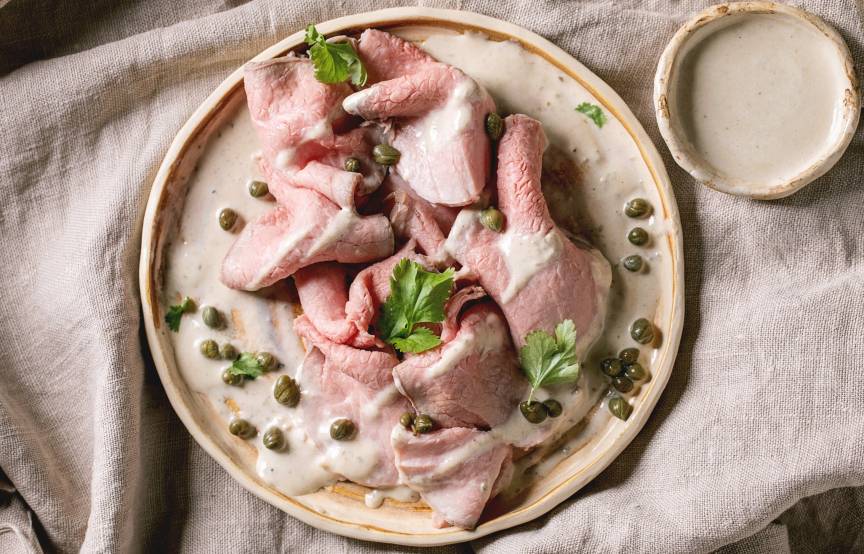 Selbstgemachtes Vitello tonnato angerichtet auf einem Vorspeisenteller, daneben Thunfischsauce und Kapern