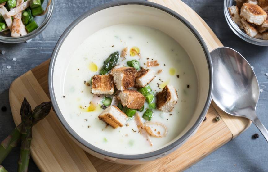 Selbstgekochte Spargelcremesuppe liebevoll angerichtet mit frischen Gewürzen und Einlagen auf einem Tisch
