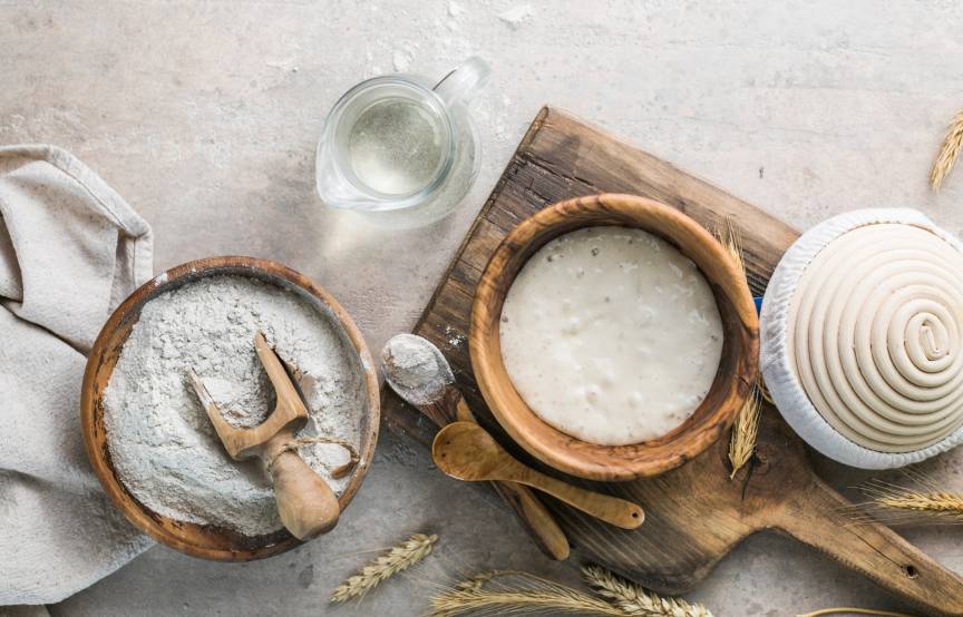 Aktiver Sauerteigstarter auf einem Tisch neben weiteren Brotbackzutaten wie Mehl und Wasser