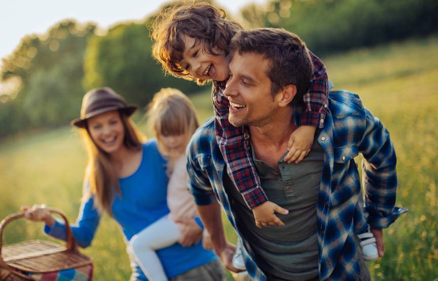 Eine Familie läuft lachend über ein Feld, die Mutter trägt einen Picknickkorb