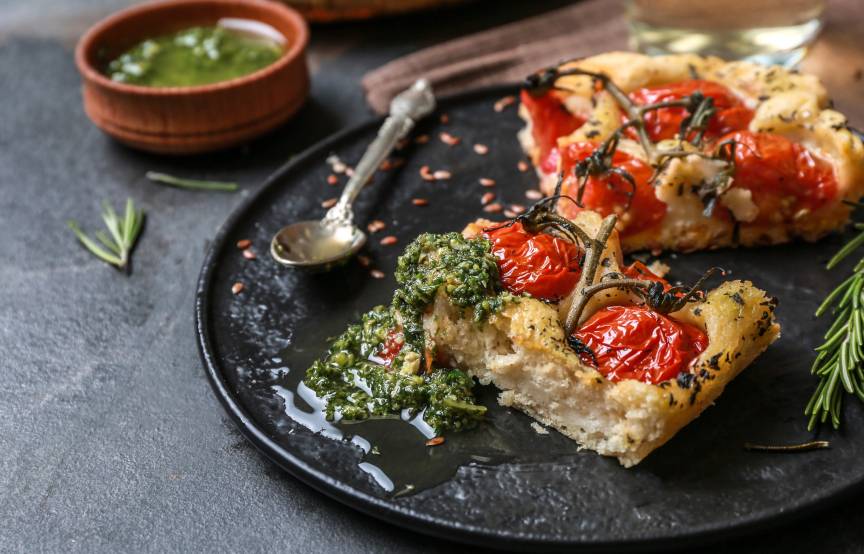 Selbstgebackene Focacciastücke belegt mit Kirschtomaten, daneben grünes Pesto als Dip