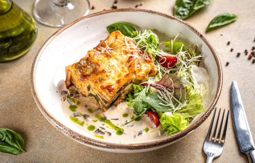 Ein Stück Lasagne angerichtet mit Salat auf einem Pastateller