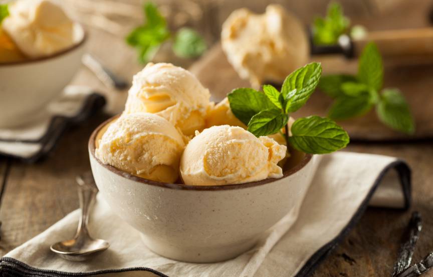 Mehrere Dessertschalen mit Vanilleeis-Kugeln garniert mit frischen Minzblättern auf einem Holztisch
