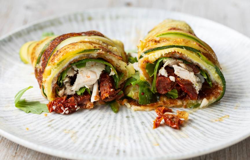 Zwei gerollte Italienische Wraps gefüllt mit Hähnchen, Zucchini und Käse angerichtet auf einem Teller