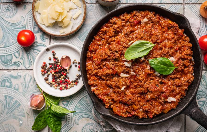 Slebstgekochte Bolognese in einer Pfanne auf einem Tisch umgeben von Zutaten