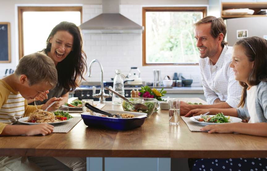 Eine vierköpfige Familie sitzt beim Abendessen an einer Kücheninsel und genießt Spaghetti