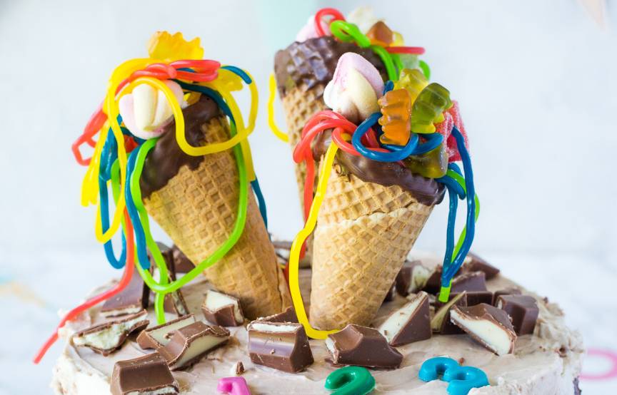 Mehrschichtige Kinder Riegel Einschulungstorte dekoriert mit bunt gefüllten Schultüten aus Eiswaffeln auf einer Tortenplatte