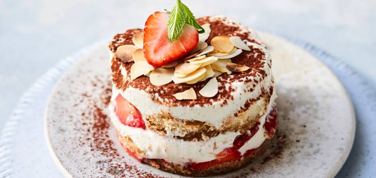 Kreisrund augestochenes Erdbeertiramisu auf einem Teller getoppt von mit Mandelblättchen
