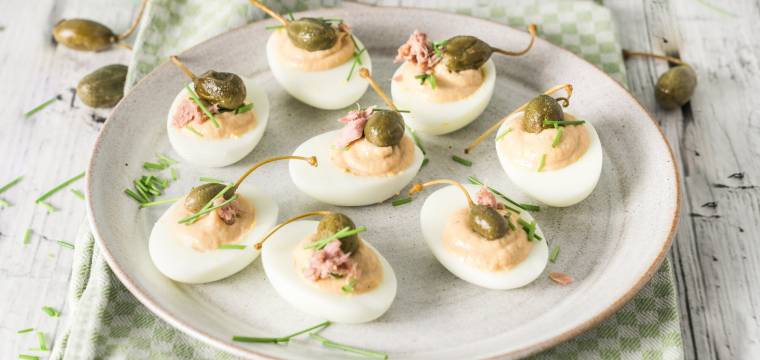 Gefüllte Eier nach Vitello-tonnato-Art auf einer Platte, daneben Kapernäpfel auf einem Tisch
