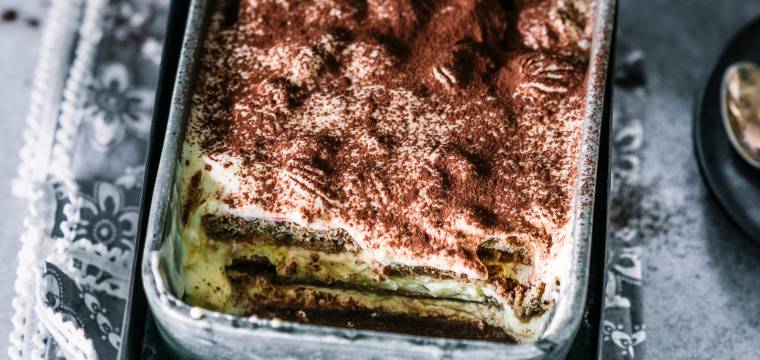Tiramisu in einer metallenen Auflaufform angeschnitten auf einem Tisch