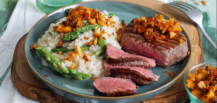 Spargelrisotto auf einem Teller, daneben Rindermedaillons aus dem Ofen getoppt mit Bröseln