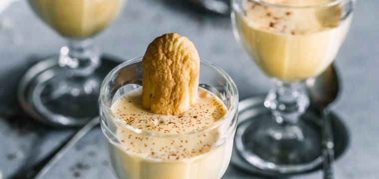 Zabaione in vier Gläsern getoppt von jeweils einem Löffelbiskuit und Marsala auf einem Tisch