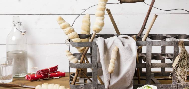 Vorbereitete Stockbrote in einem Metallkorb auf einem Holztisch