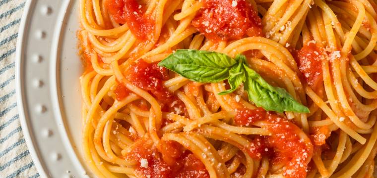Spaghetti al pomodoro angerichtet auf einem weißen runden Teller garniert mit frischem Basilikum