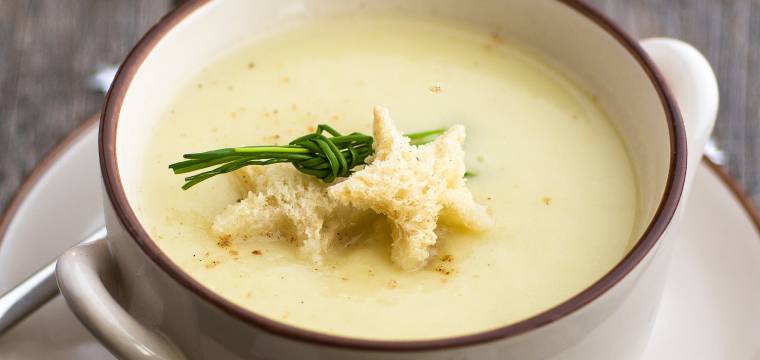 Weihnachtssuppe in einer Suppentasse getoppt mit Sternen aus Brot und Schnittlauch auf einem festlichen Tisch