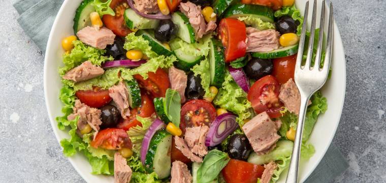 Thunfischsalat mit Mais, Oliven, Gurke, Zwiebel und Tomate auf einem Teller garniert mit frischer Petersilie