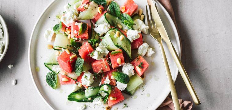 Wassermelonen-Feta-Salat mit Gurke auf einem Teller getoppt von Minzblättern und Pinienkernen