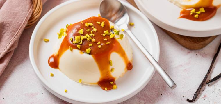 Drei Vanille-Panna-cotta übergossen mit Karamellsoße und getoppt von gehackten Pistazien auf Desserttellern Drei Vanille-Panna-cotta übergossen mit Karamellsoße und getoppt von gehackten Pistazien auf Desserttellern