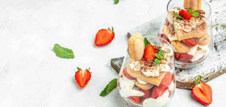 Zwei Gläser mit Erdbeer-Tiramisu mit Mascarpone und Quark garniert mit frischen Minzblättern auf einem Tisch Zwei Gläser mit Erdbeer-Tiramisu mit Mascarpone und Quark garniert mit frischen Minzblättern auf einem Tisch