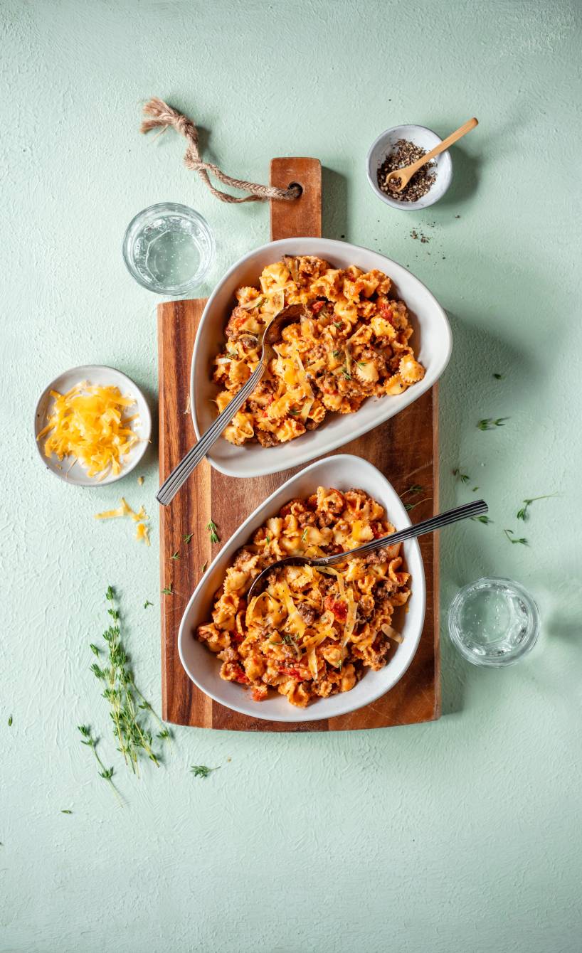 One Pot Pasta mit Bolognese in zwei tiefen Tellern, daneben Käseraspel in einer Schüssel