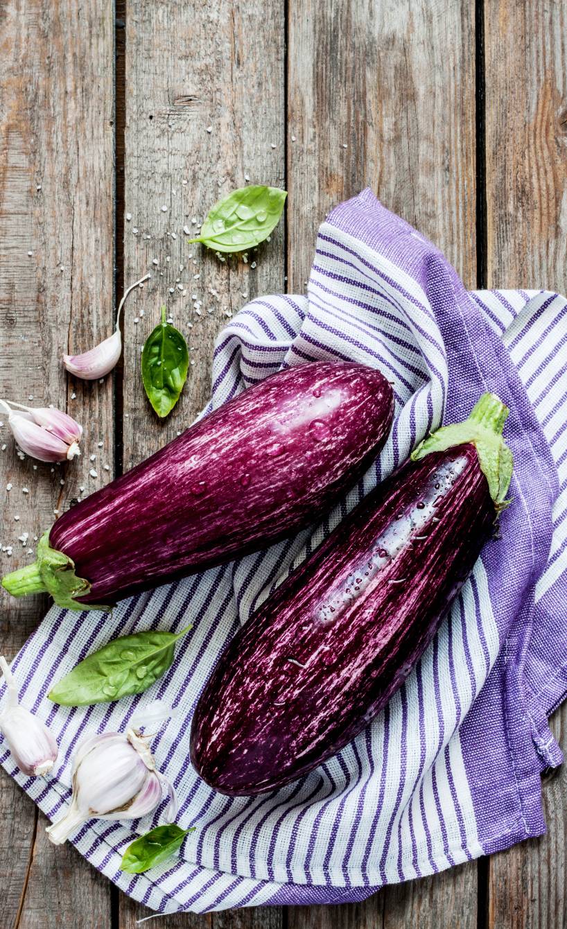 Zwei lilafarbene Auberginen auf einem Küchenhandtuch und Holzuntergrund