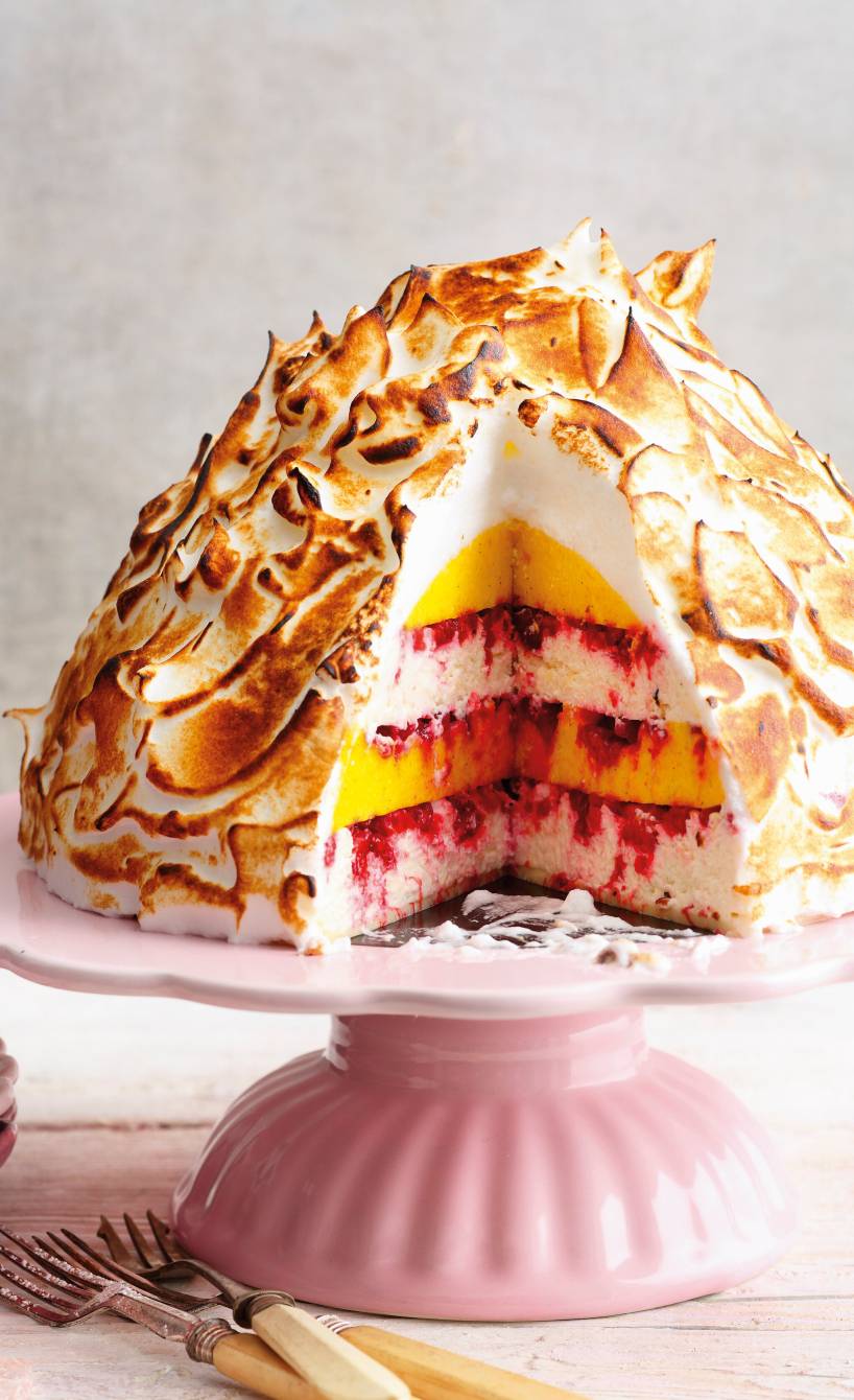 Mango-Kokos-Eisbombe mit Himbeeren und flambierter Baiser-Haube angeschnitten auf einer Tortenplatte