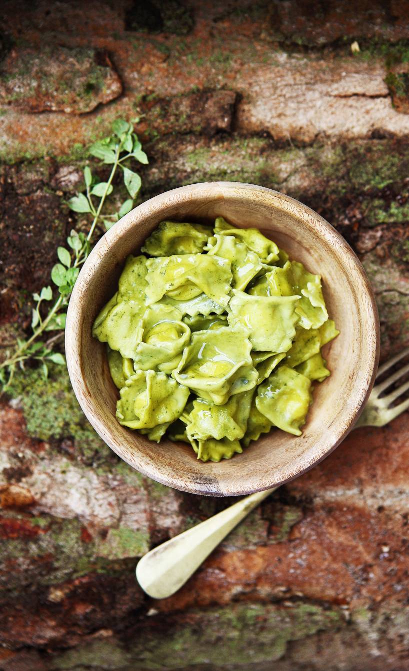 Agnolotti in einem tiefen Teller auf einem Holztisch, daneben ein Zwei Kräuter