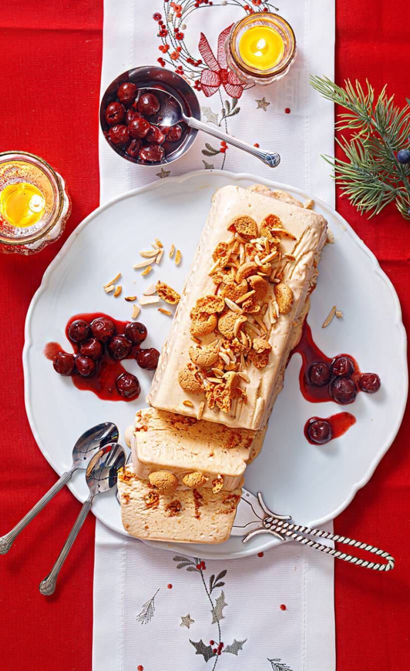 Amarettini-Semifreddo getoppt mit Glühweinkirschen auf einer Servierplatte auf einem weihnachtlich dekorierten Tisch
