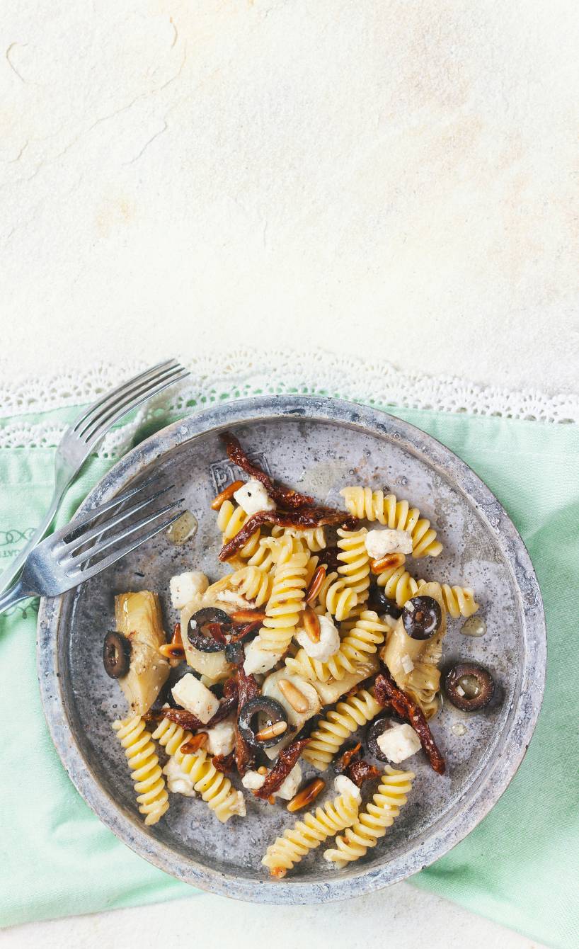 Antipasti-Nudelsalat auf einem Teller getoppt mit Stücken von Büffelmozzarella