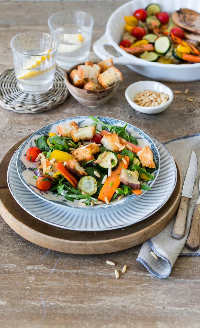 Antipasti-Salat angerichtet auf zwei Teller getoppt mit Croûtons und Pinienkernen