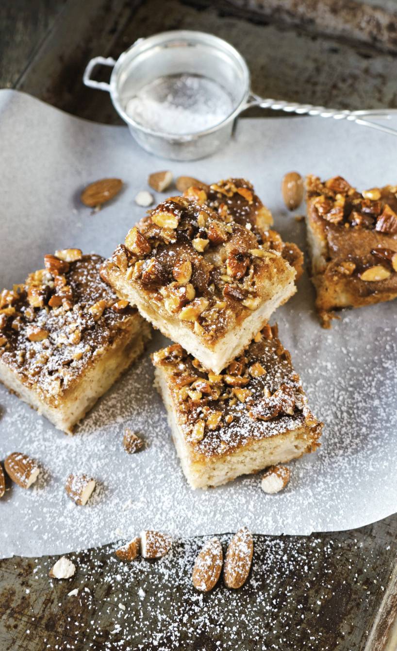 Fünf quadratisch Stücke Apfelkuchen vom Blech mit Zimtmandelhaube auf einem Stück Backpapier