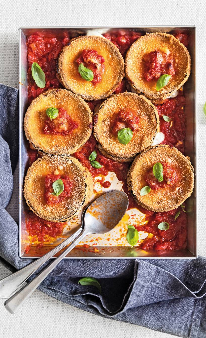 gebackene, panierte Aubergine-Taler mit Caciocavallo-Kruste auf einem Backblech mit Sugo und Basilikumblättern angerichtet