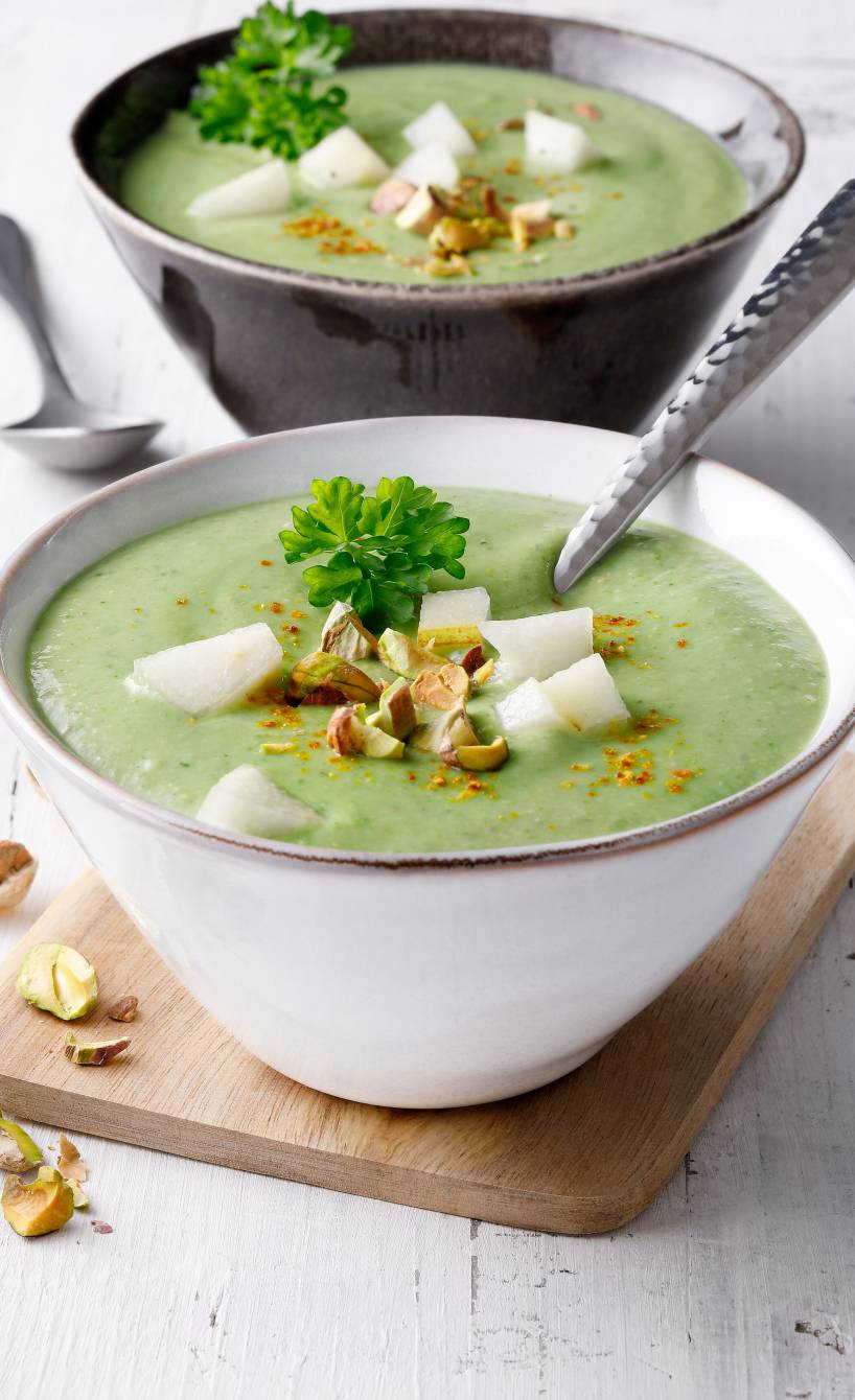 Cremige Spinat-Suppe mit Avocado getoppt von Birnenstücken und gehackten Pistazien in zwei Suppenschalen
