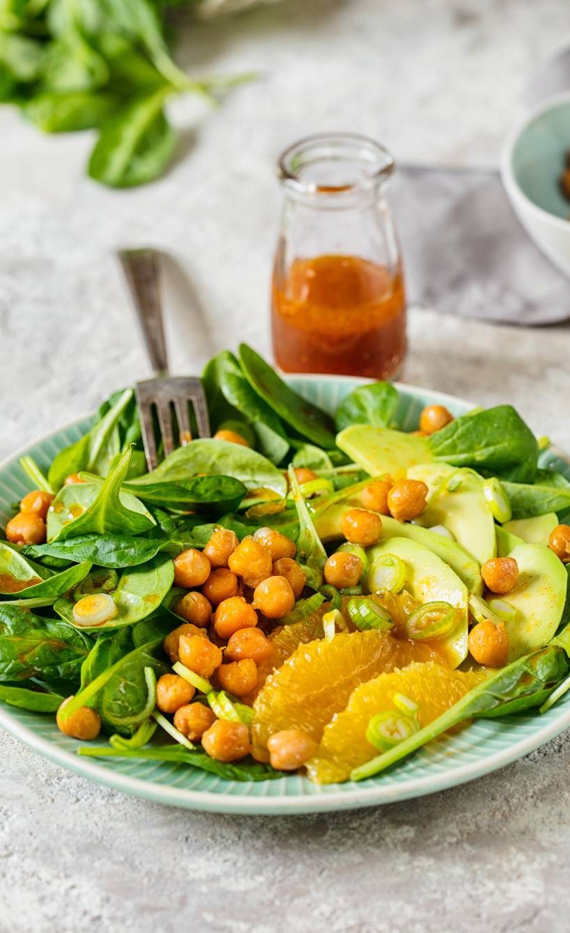 Spinat-Salat mit gebackenen Kichererbsen, Avocadostreifen und  Orangenfilets angerichtet auf einem Teller