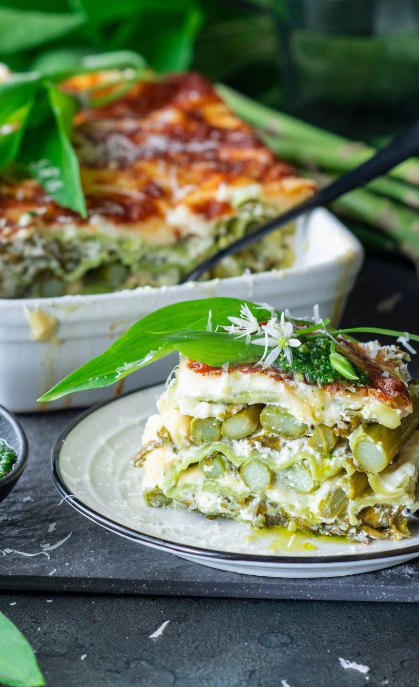 Bärlauch-Spargel-Lasagne in einer Auflaufform, davor ein Stück auf einem Teller