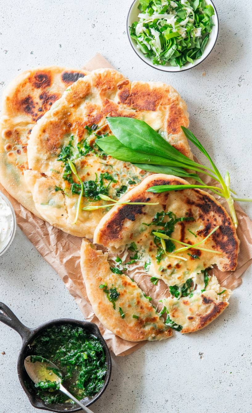 Gefüllte Fladenbrote auf einem Stück Backpapier, daneben Bärlauch-Käse-Mix in einer Schüssel