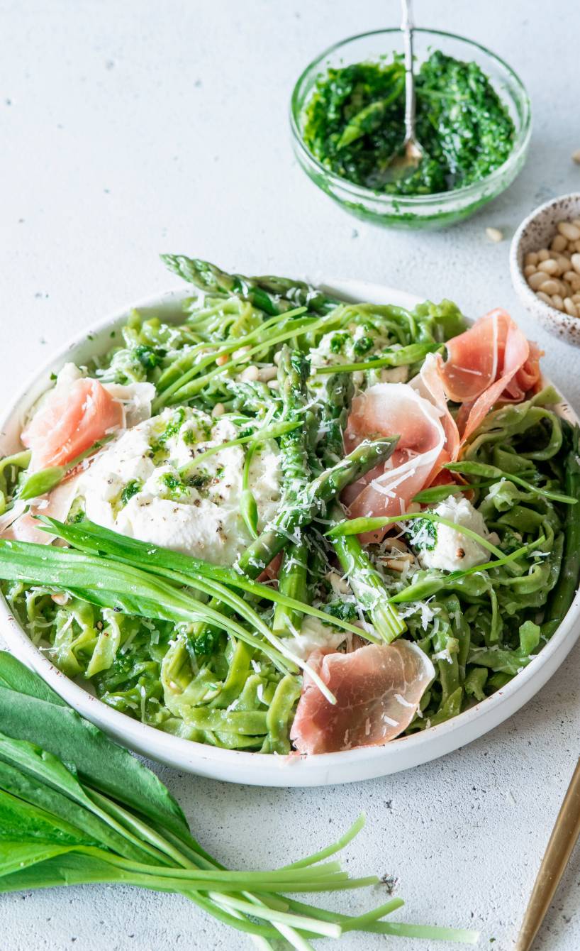 Grüne Tagliatelle mit Bärlauchpesto, grünem Spargel, Mozzarlla und Parmaschinken in einem tiefen Teller