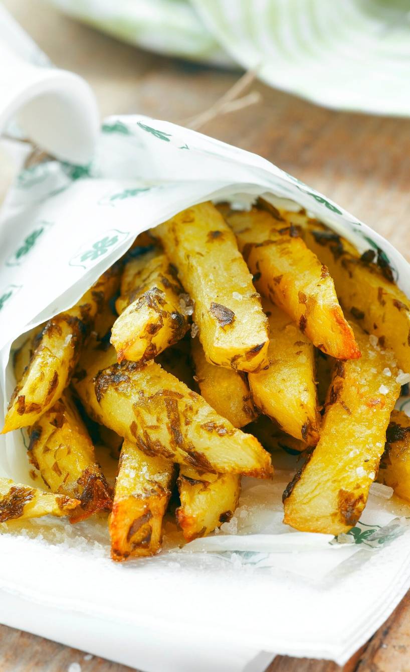Kartoffelsticks in einer Papiertüte auf einem Holztisch, daneben Salsa und Basilikum