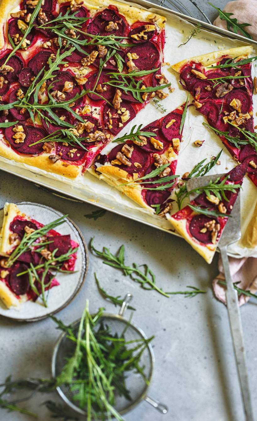 rechteckige Blätterteig-Pizza mit Rote Bete, Rucola, Ziegenkäse und Walnüssen angeschnitten auf einem Backblech