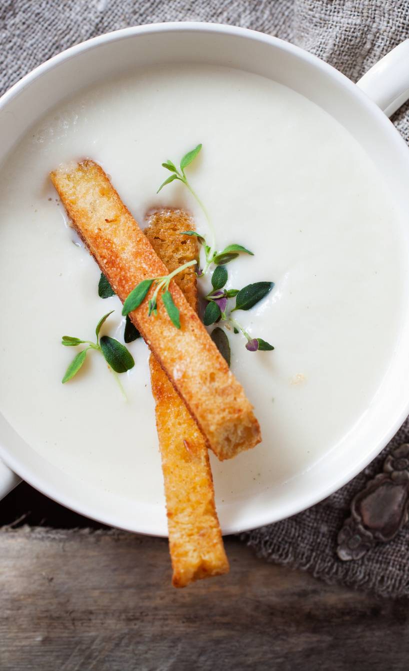 Blumenkohlcremesuppe garniert mit Brotsticks und frischen Kräutern in einer Suppenschale