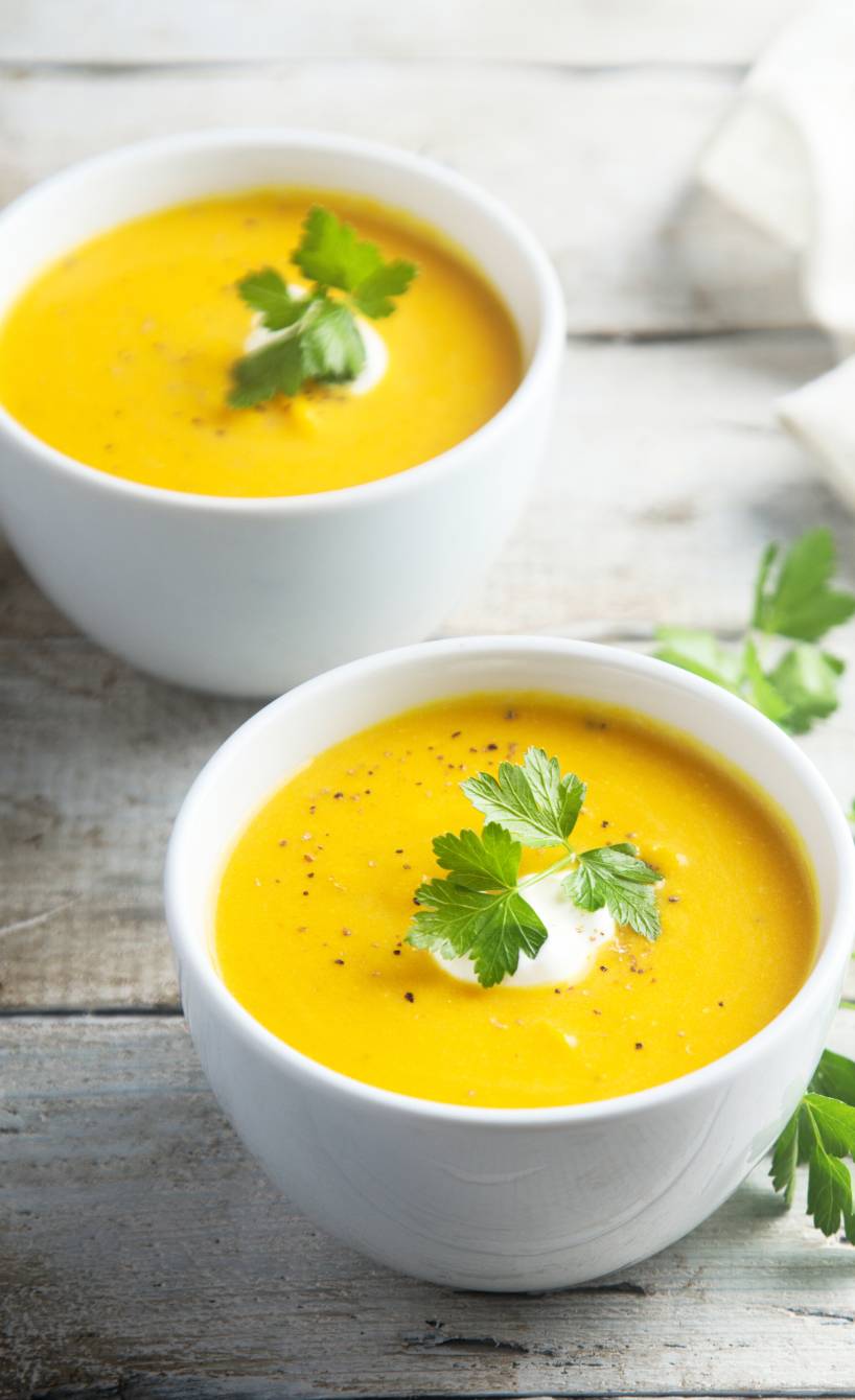 Gelbe Blumenkohlsuppe in zwei Schalen garniert mit frischen Kräutern auf einem Tisch