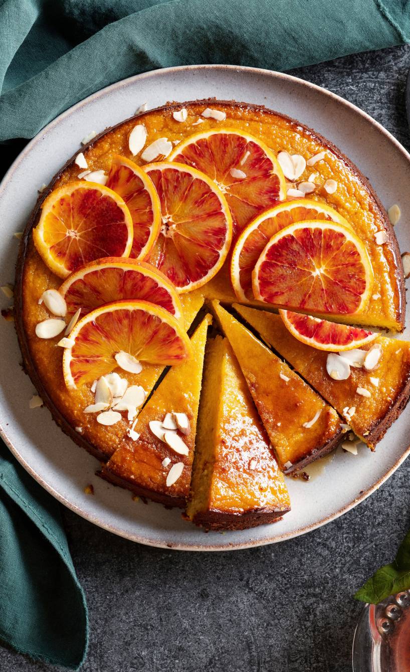 Runder glutenfreier Mandel-Kuchen belegt mit Blutorangenscheiben angeschnitten auf einer Kuchenplatte
