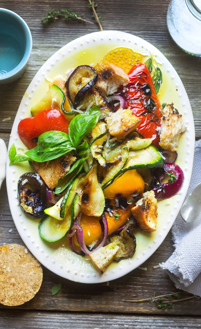 Italienischer Brotsalat mit Grillgemüse auf einem ovalen Teller garniert mit frischem Basilikum