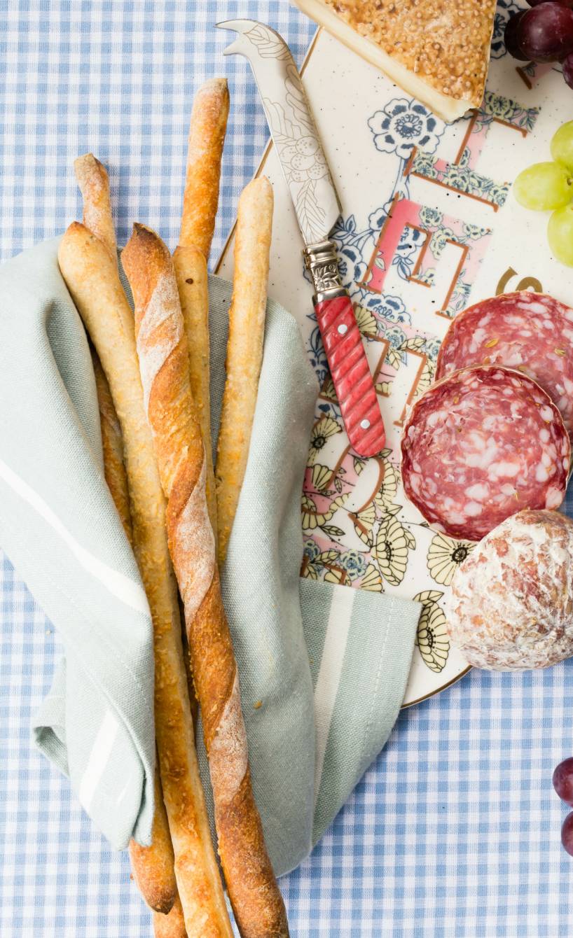 Selbstgebackene italienische Brotsticks auf einer Snackplatte mit Käse, Weintrauben und Salami