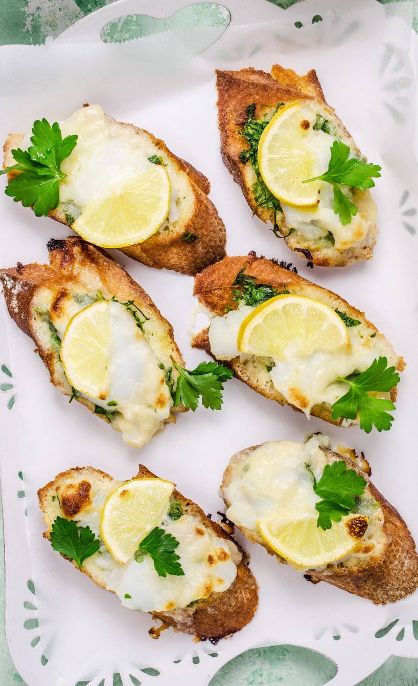 Bruschetta mit Kabeljau, Mozzarella und Zitrone auf einem Tablett garniert mit frischer Petersilie