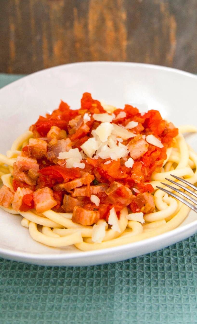 Bucatini-Nudeln in einem tiefen Teller mit Sauce all’amatriciana auf einem Tisch