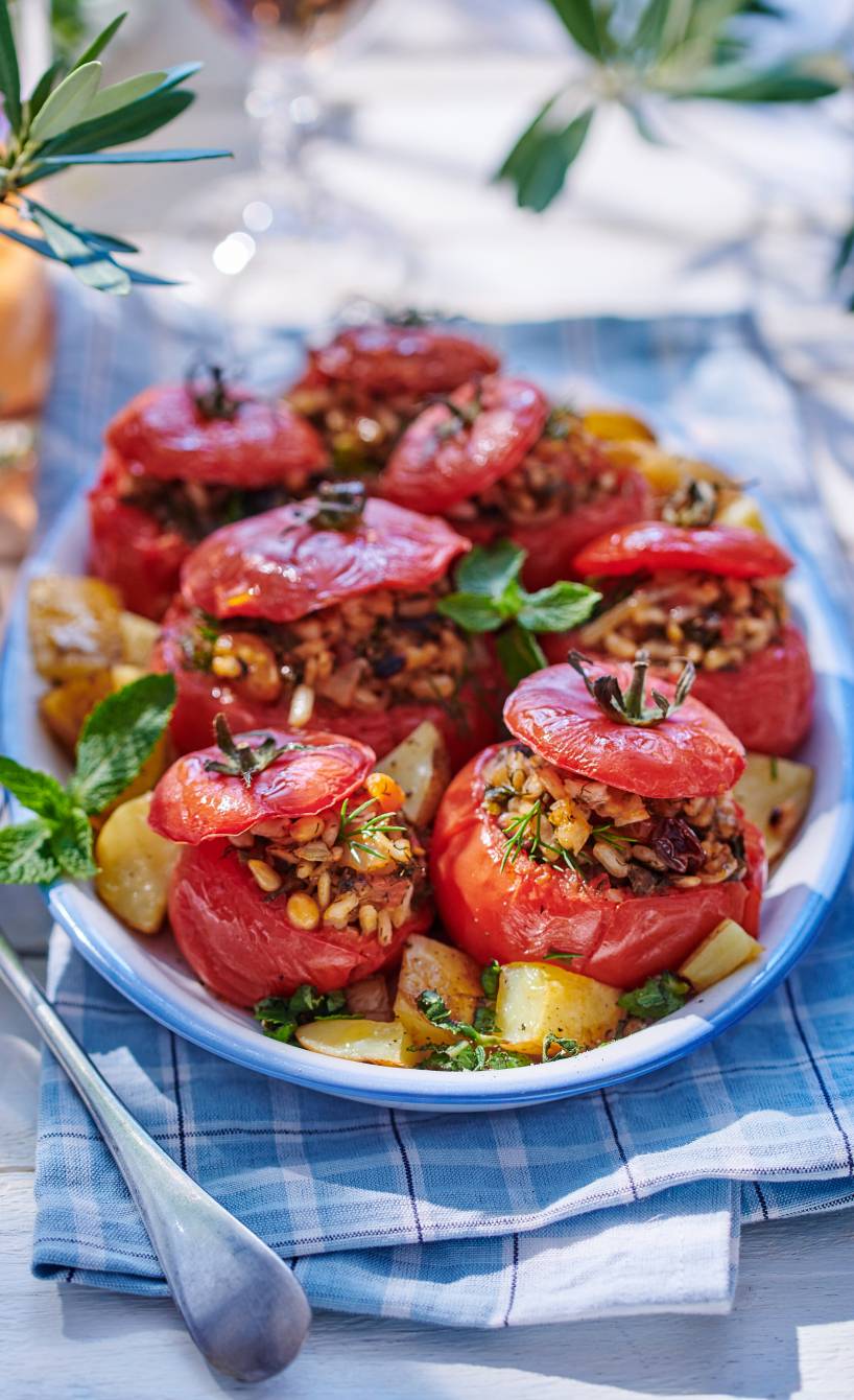 Gebackene, vegan gefüllte Tomaten auf einer Servierplatte umgeben von Kartoffeln aus dem Ofen