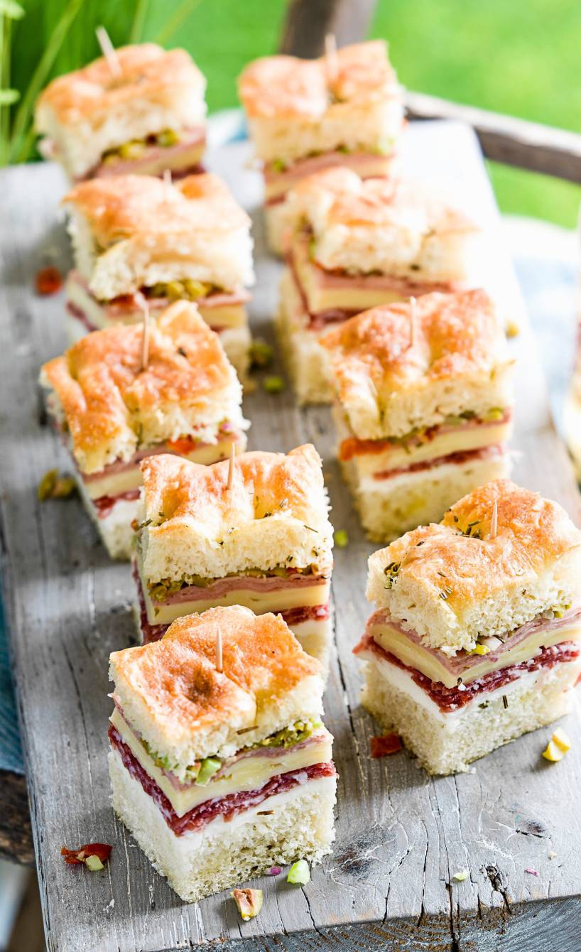 Focaccia-Würfel mit üppigem Belag auf einem Holzbrett, daneben Drinks