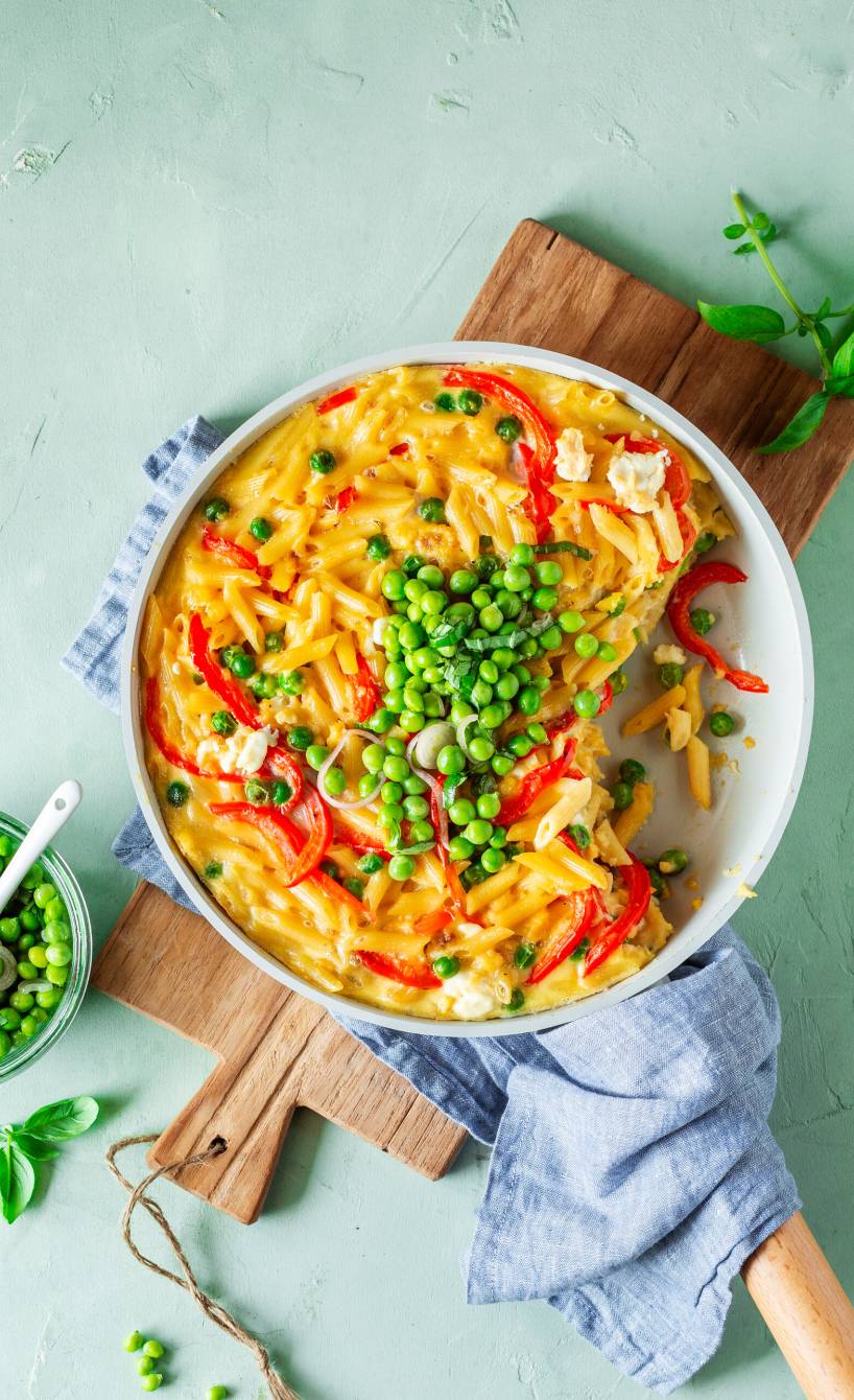 Pfanne mit Frittata mit Feta, Nudeln und Paprika getoppt von Erbsensalat auf einem Holzbrett